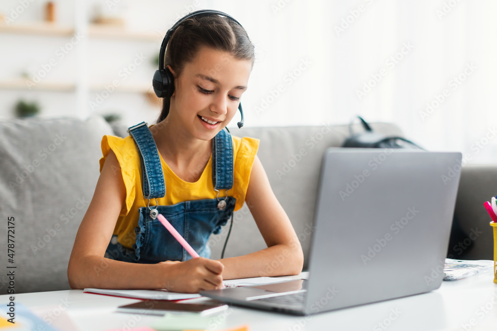 Girl using laptop, having videocall with teacher, writing in notebook Girl using laptop, having videocall with teacher, writing in notebook