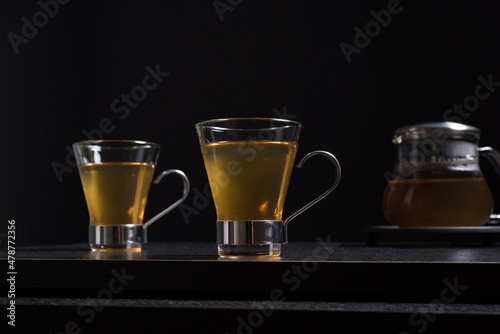 Dos tazas de té caliente de jengibre con tetera sobre una mesa de madera negra