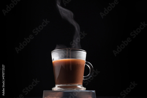 Café caliente y humeante en taza de vidrio sobre fondo negro. Aislado