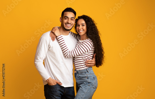 Portrait of joyful romantic middle-eastern couple embracing while posing over yellow background
