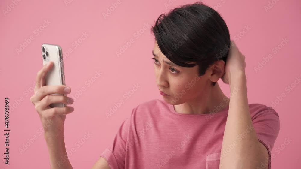 Serious Asian man correcting his hairstyle by phone in the pink studio Serious Asian man correcting his hairstyle by phone in the pink studio