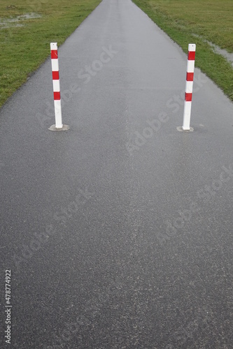 Tarmac hike and bike path with red and white metal traffic poles (vertical image), Burhave, Lower Saxony, Germany © Jens