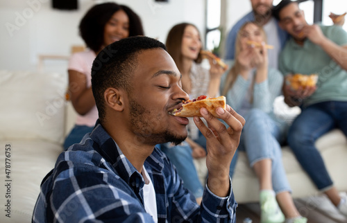 Funky black guy eating tasty pizza with his multinational friends, enjoying social gathering at home