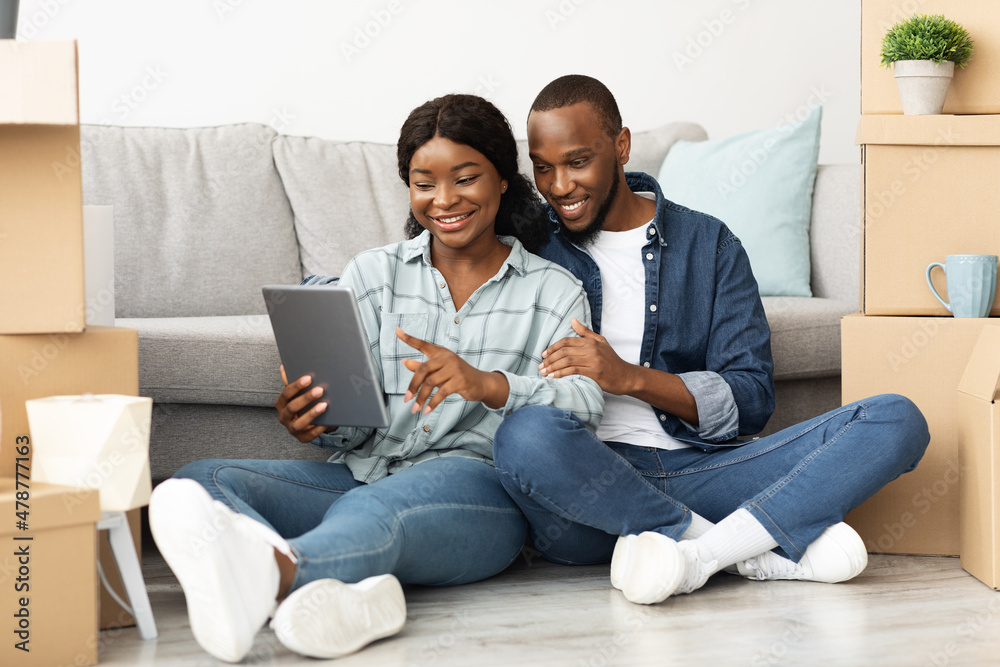 Black Spouses With Digital Tablet Sitting Among Cardboard Boxes In New Flat Black Spouses With Digital Tablet Sitting Among Cardboard Boxes In New Flat