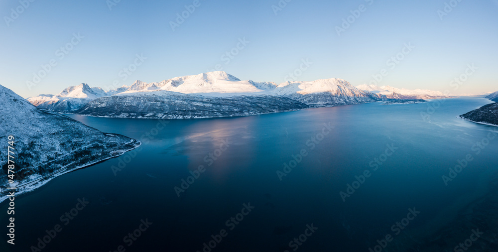 Aerial drone view of a snowy and icy lake in Norway during sunset
