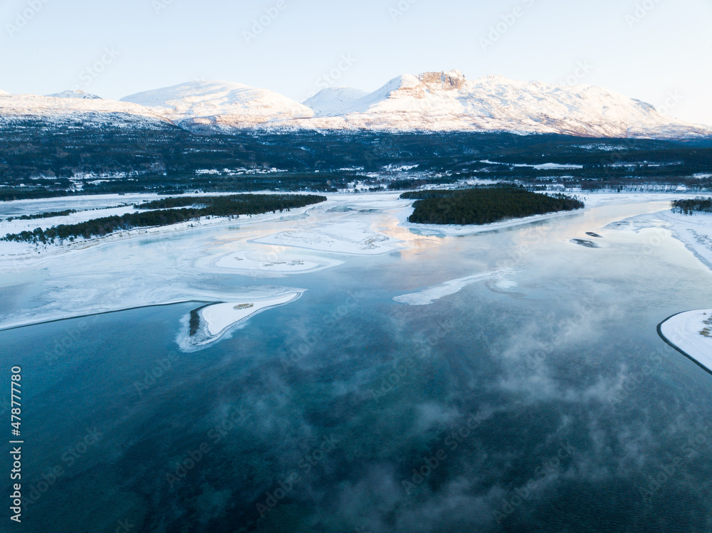 Aerial drone view of a snowy and icy lake in Norway during sunset