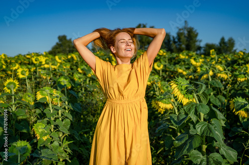 A young beautiful, happy, caucasian girl squints from the sunlight, rejoices, throws her hair up in a sunflower field