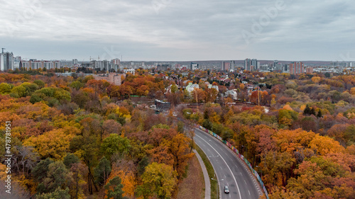 Aerial scenic road curve in autumnal residential district. Fly above street in autumn city park with cloudy epic sky. Treetop view on Kharkiv, Ukraine