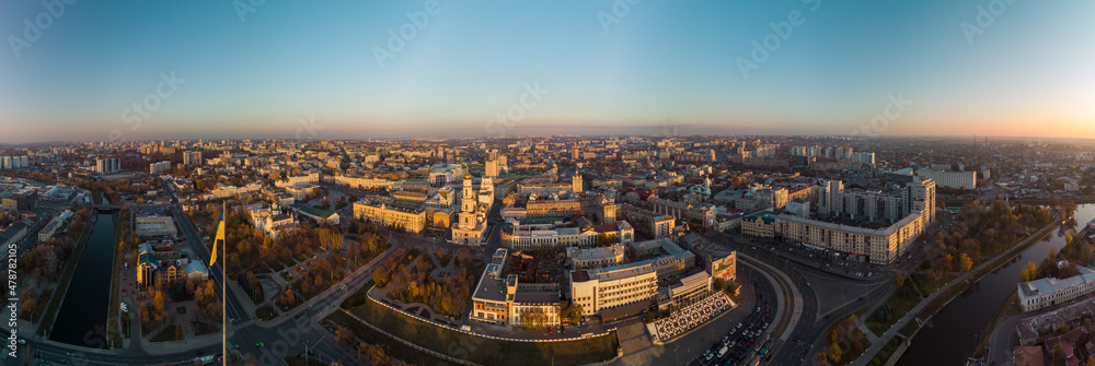 Obraz premium Sunny autumn cityscape, city streets traffic. Wide panoramic aerial view above river Lopan embankment, Flagpole with flag of Ukraine, Pavlivska Square, Dormition Cathedral in Kharkiv, Ukraine
