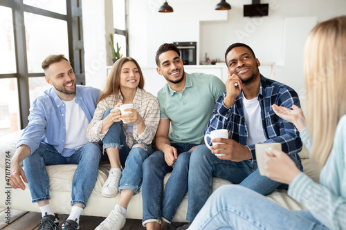 Multiethnic young friends enjoying conversation, drinking tea or coffee at home