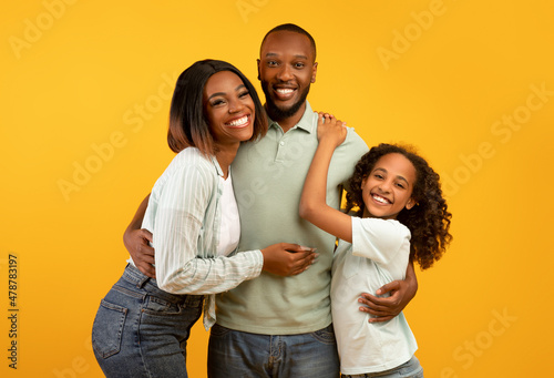 Portrait of happy african american family of mother, father and their little daughter posing over yellow background