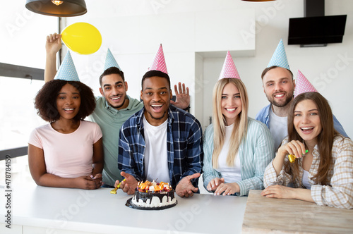 Diverse young friends making surprise with cake and canles for black birthday guy, throwing party at home photo