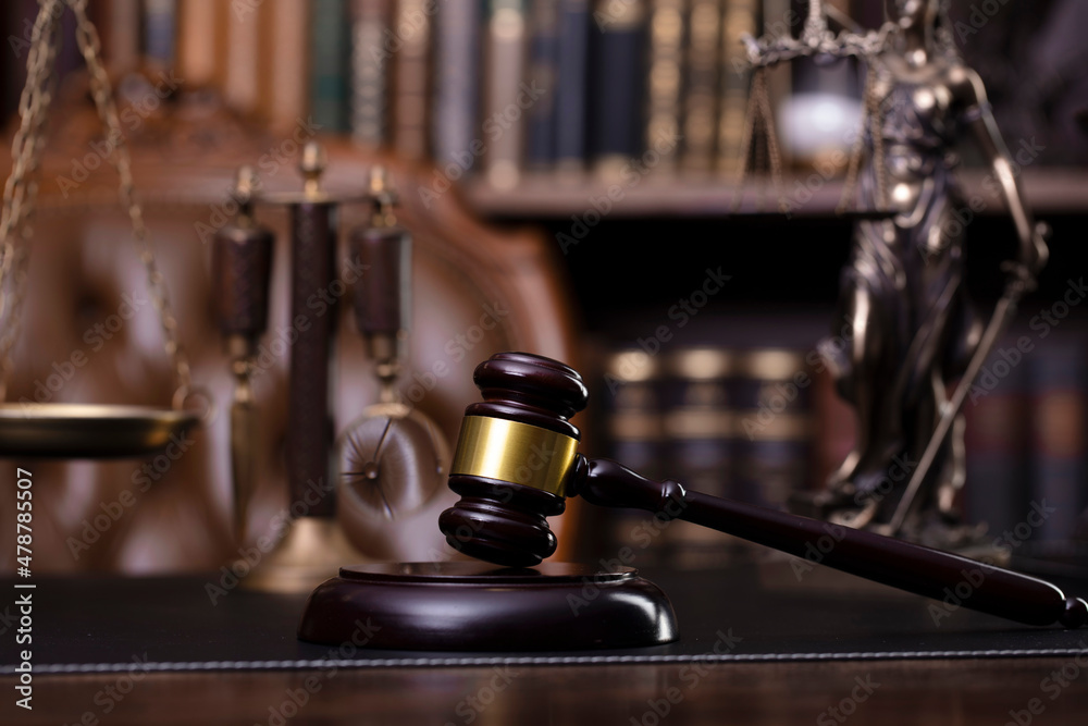 Judge office. Gavel, scale, Themis sculpture on the desk. Law books in the bookshelf.
