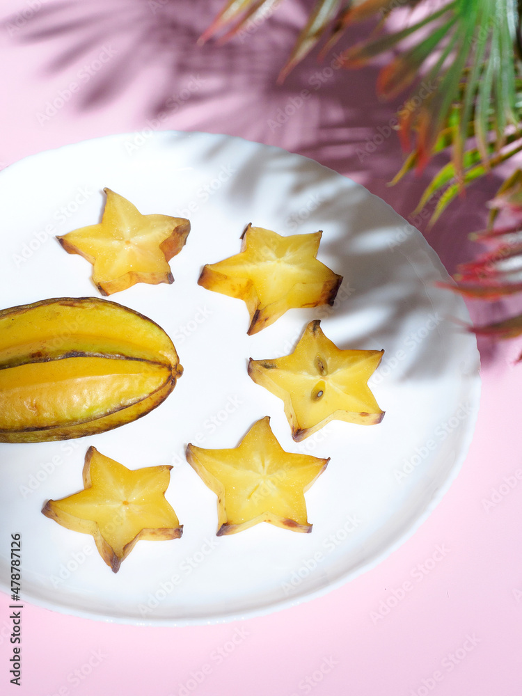 Fototapeta premium Cut and whole carambolas with green palm leaves on white background. Flat lay composition with carambolas on color pink background. Top view. Yellow exotic tropical fruits. Copy spase. Space for text.