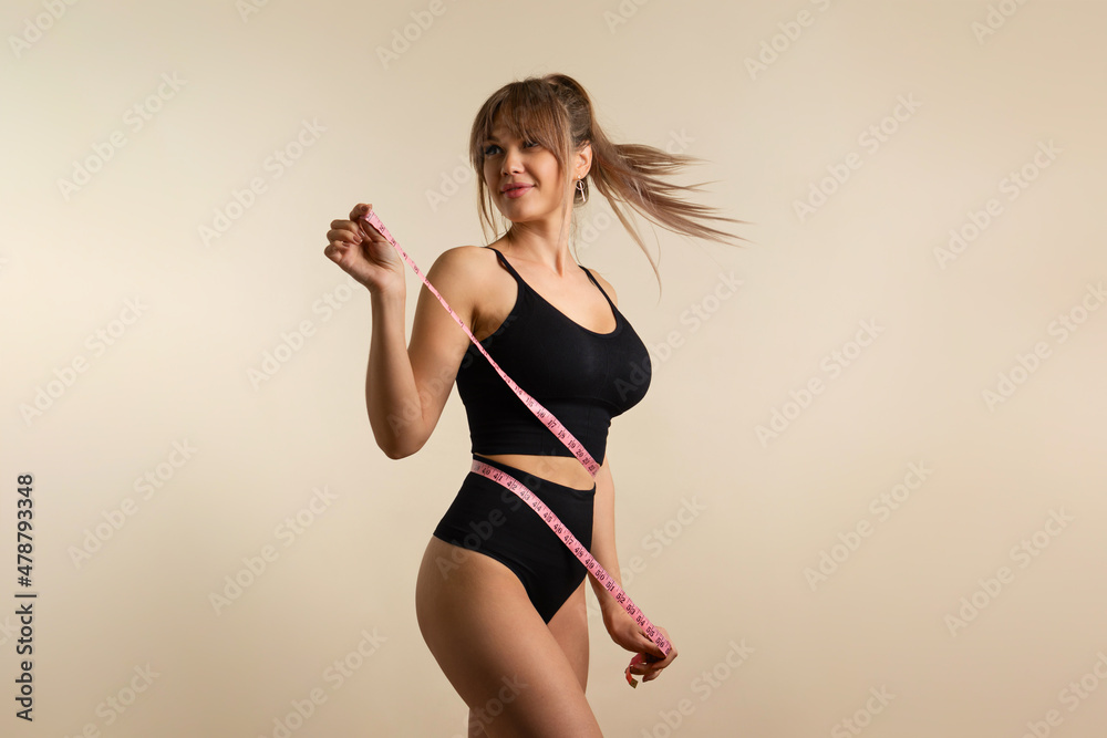Slim healthy girl in black underwear with measuring tape at waist. Fit  Woman poses in high