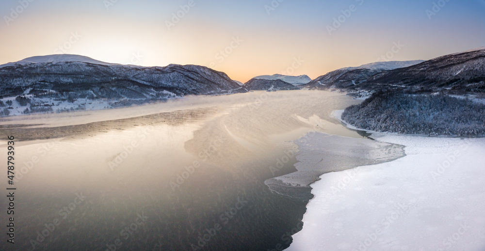 Aerial drone view of a snowy and icy lake in Norway during sunset