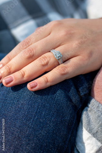 Close up of females hand with engagement ring shining in the sunlight.  Hand resting on blue jeans with sun shining outdoors.  