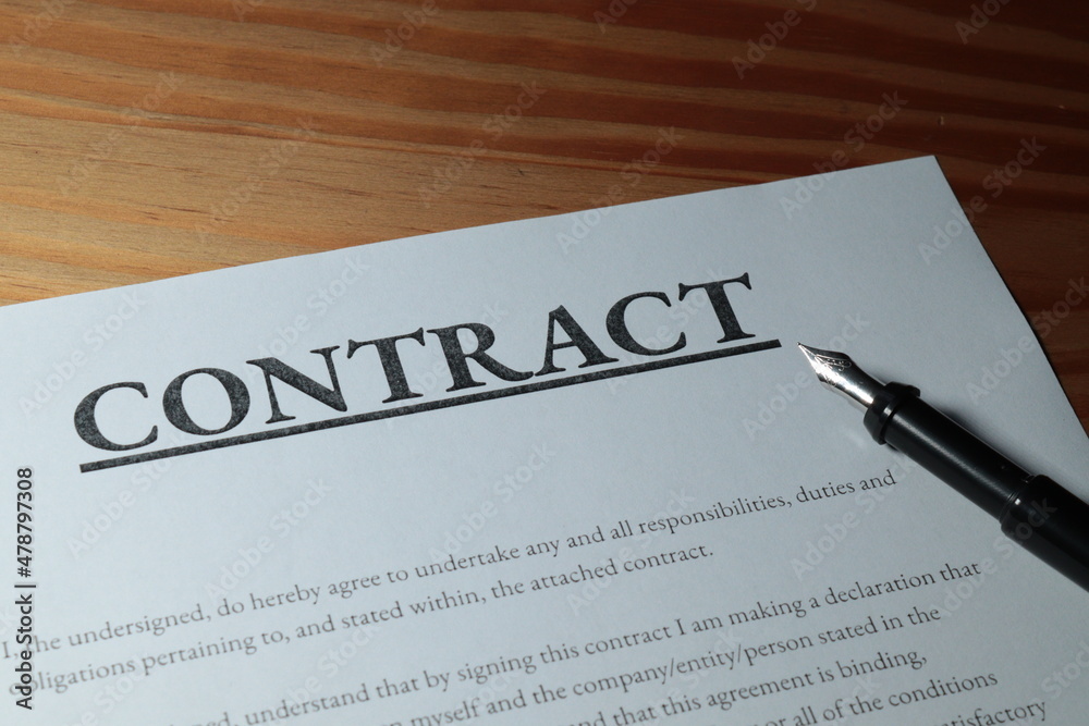 Fountain pen lain across contract paperwork against wooden table top Fountain pen lain across contract paperwork against wooden table top