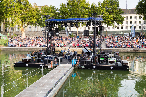 Spectacle musical sur une scène flottant sur une rivière, avec nombreux spectateurs sur des gradins. RDV de l'Erdre, Nantes