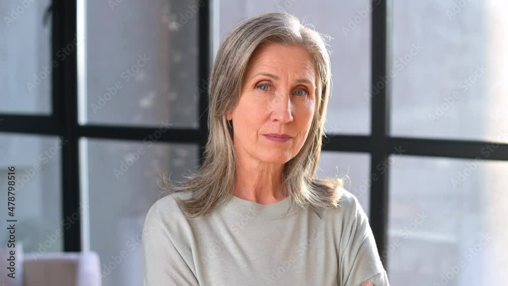 Portrait of an elegant stylish mature middle-aged gray-haired businesswoman, ceo in glasses standing in the modern office posing and looking at the camera Portrait of an elegant stylish mature middle-aged gray-haired businesswoman, ceo in glasses standing in the modern office posing and looking at the camera