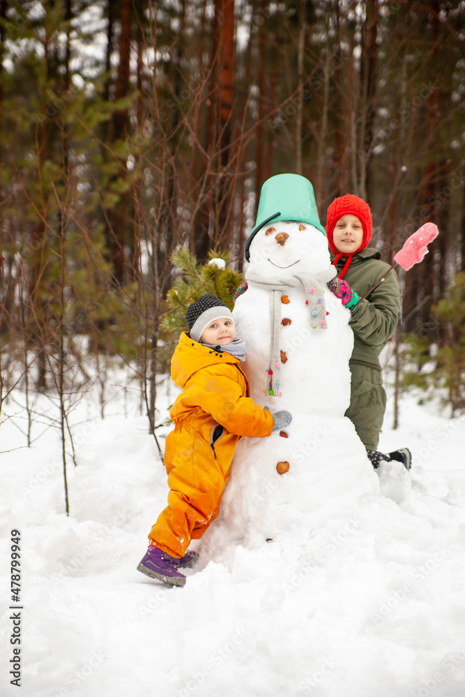 Two sisters making  snowman  in winter  forest