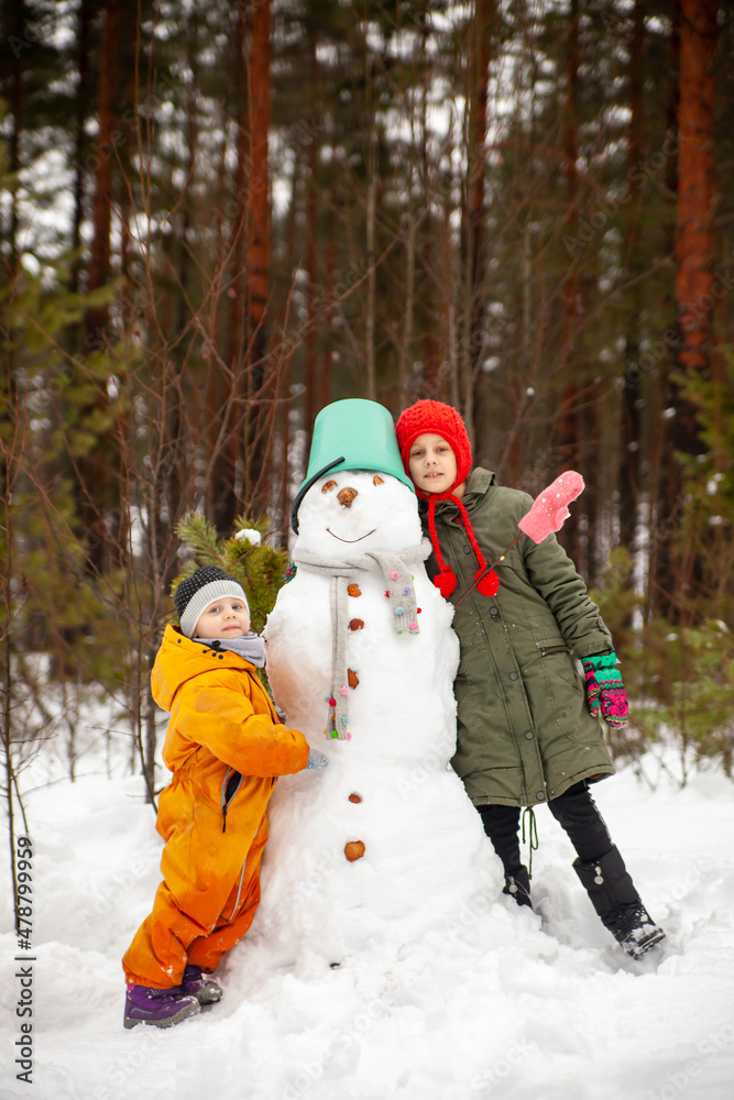 Two sisters making  snowman  in winter  forest