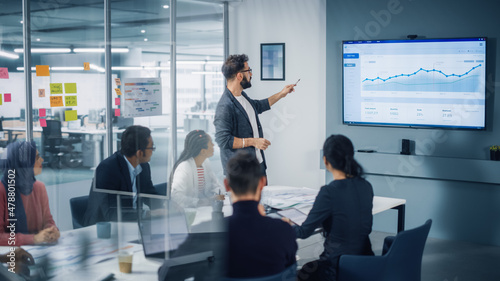 Diverse Modern Office: Motivated Businessman Leads Business Meeting with Managers, Talks, uses Presentation TV with Statistics, Chart Growth, Big Data. Digital Entrepreneurs Work on e-Commerce Project photo
