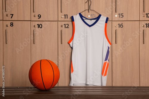 Photography Orange basketball ball on wooden bench and hanger with uniform in locker room