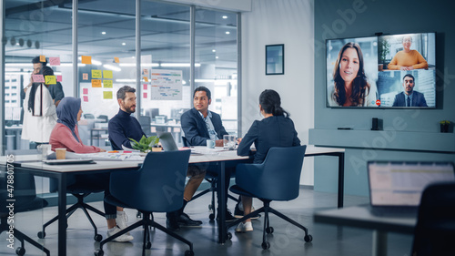 Businesspeople do Video Conference Call with Big Wall TV in Office Meeting Room. Diverse Team of Creative Entrepreneurs at Big Table have Discussion. Specialists work in Digital e-Commerce Startup photo