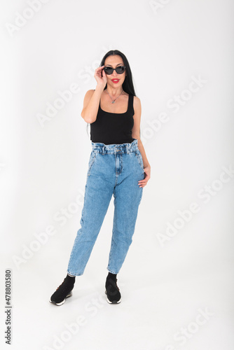 A stylish woman with a southern or oriental appearance in a studio on a white background in sunglasses and jeans