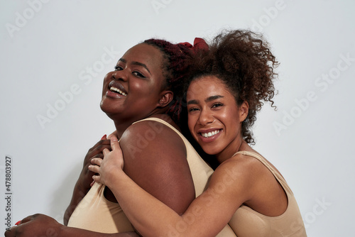 Portrait of two african american women in underwear with different body size having fun while posing together isolated over gray background