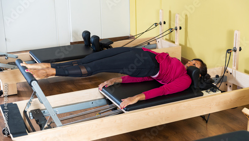 Hispanic woman performing pilates on reformer in fitness studio