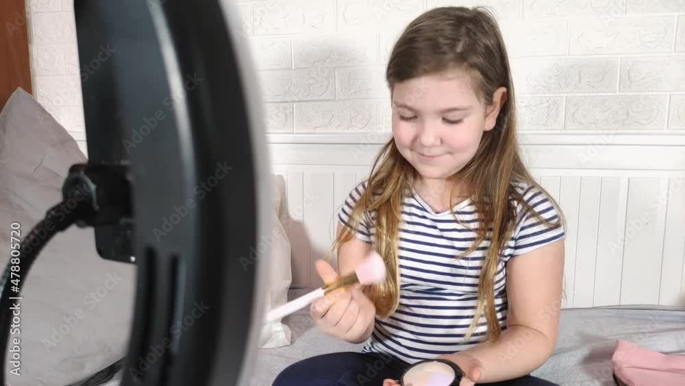 Technology and beauty vlog for kids. Cute Caucasian blogger girl doing makeup, showing cosmetics and face powder. Girl Recording Blog, Talking to Camera Technology and beauty vlog for kids. Cute Caucasian blogger girl doing makeup, showing cosmetics and face powder. Girl Recording Blog, Talking to Camera