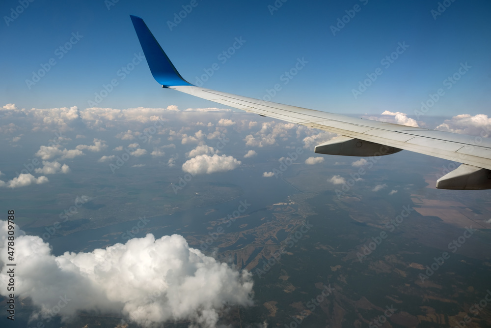 View of jet airplane wing from inside flying over white puffy clouds in blue sky. Travel and air transportation concept View of jet airplane wing from inside flying over white puffy clouds in blue sky. Travel and air transportation concept