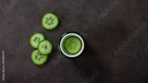 Cosmetic cream in a green jar with a vegetable cucumber on a black stone background