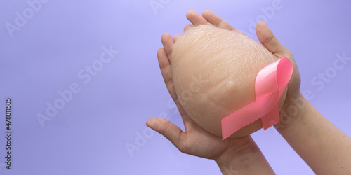 Silicone breast prosthesis on woman hands and Pink Ribbon. Breast Cancer Concept. Copy space