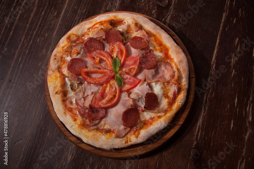 Top view shot of delicious pizza with sliced salami and ham served on wooden table