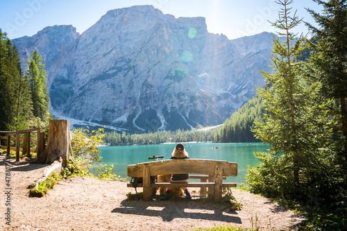 Canvas-taulu young woman sitting on a bench at pragser wildsee in the forest of the dolomites