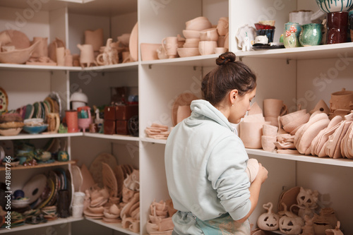 Rear view shot of a female potter standing in front of shelves with terracotta clay ware
