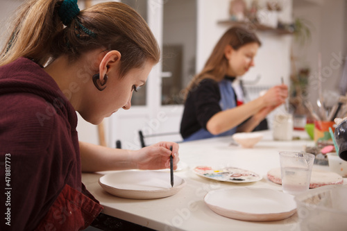 Woman drawing on a ceramic plate, working at pottery scool