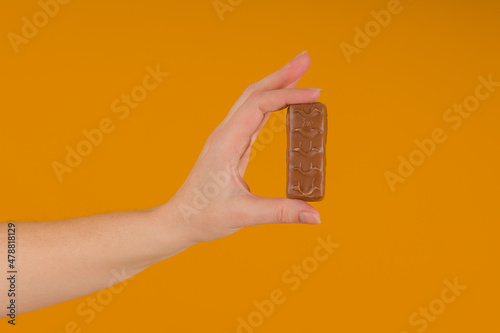 chocolate bar in a female hand on a yellow background