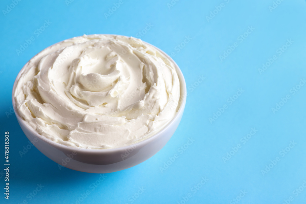 Bowl of tasty cream cheese on light blue background, space for text Bowl of tasty cream cheese on light blue background, space for text