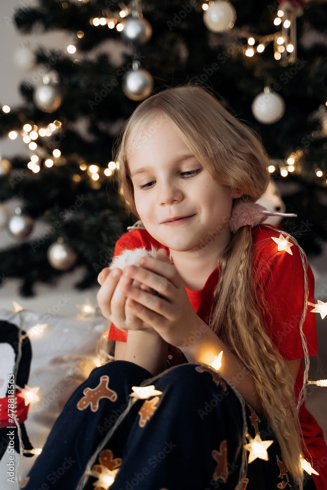 A teenage girl in a red festive T-shirt sitting with a hamster in her hands at the Christmas tree