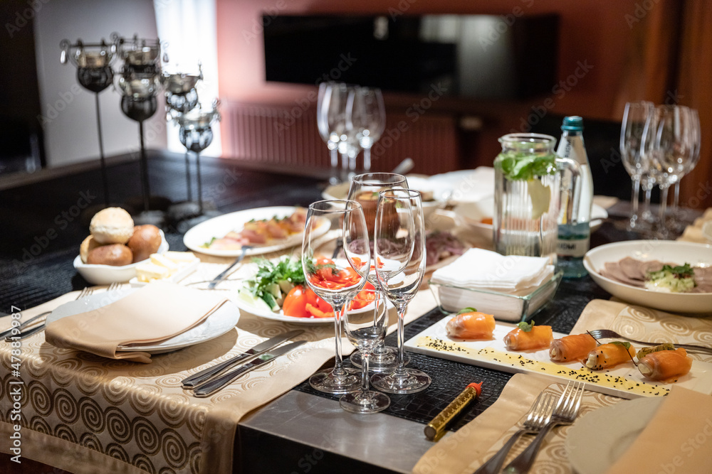 Table setting for a banquet or celebration.Empty glasses for alcoholic beverages, wine and juice, set the table.Cloth napkins on a white platter and cutlery on the table.Cold appetizers and salads