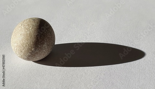 Perfectly round pebble illuminated from the left, casting an elongated shadow