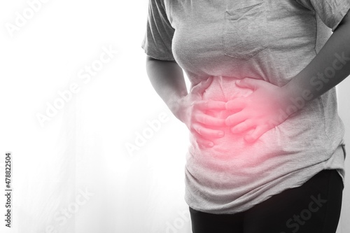 Woman wearing gray shirt has abdominal pain caused by flatulence.