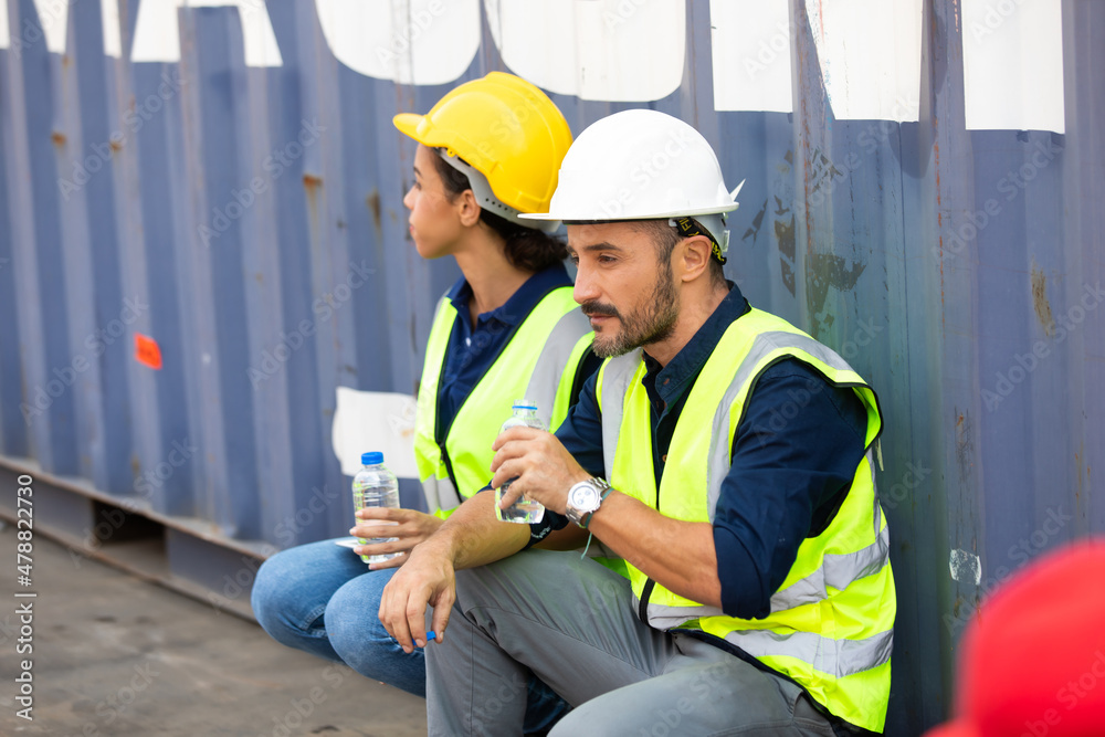 Tired hispanic male and female container worker in hardhat and uniform resting at container yard port of import and export. Tired hispanic male and female container worker in hardhat and uniform resting at container yard port of import and export.