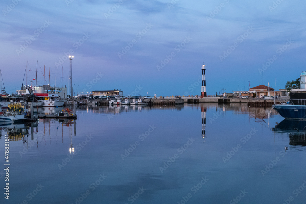 The port of Cattolica with the boats and the lighthouse reflecting in the water at sunset