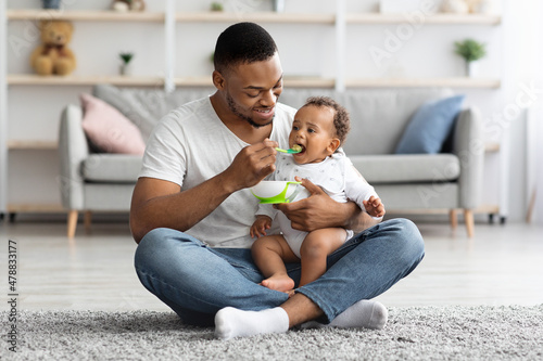 Caring Black Dad Feeding His Adorable Infant Baby From Spoon At Home