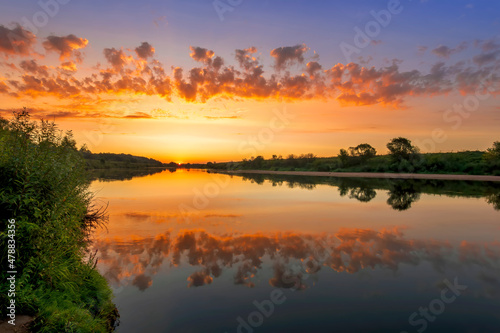 Amazing view at scenic landscape on a beautiful river and colorful sunset with reflection on water surface and glow on a background  spring season landscape